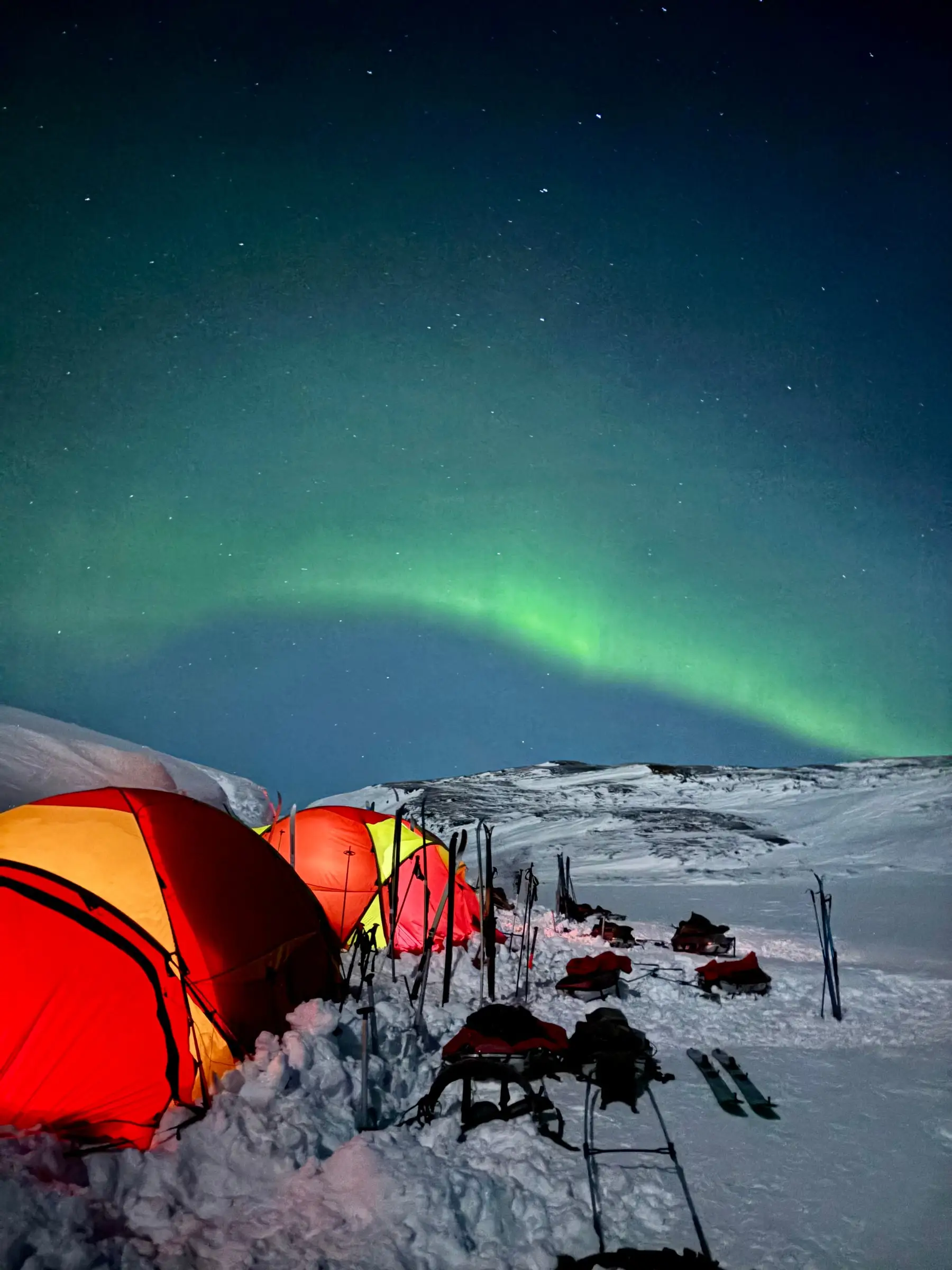 The aurora over a winter camp, tents, skis and pulks on the snow