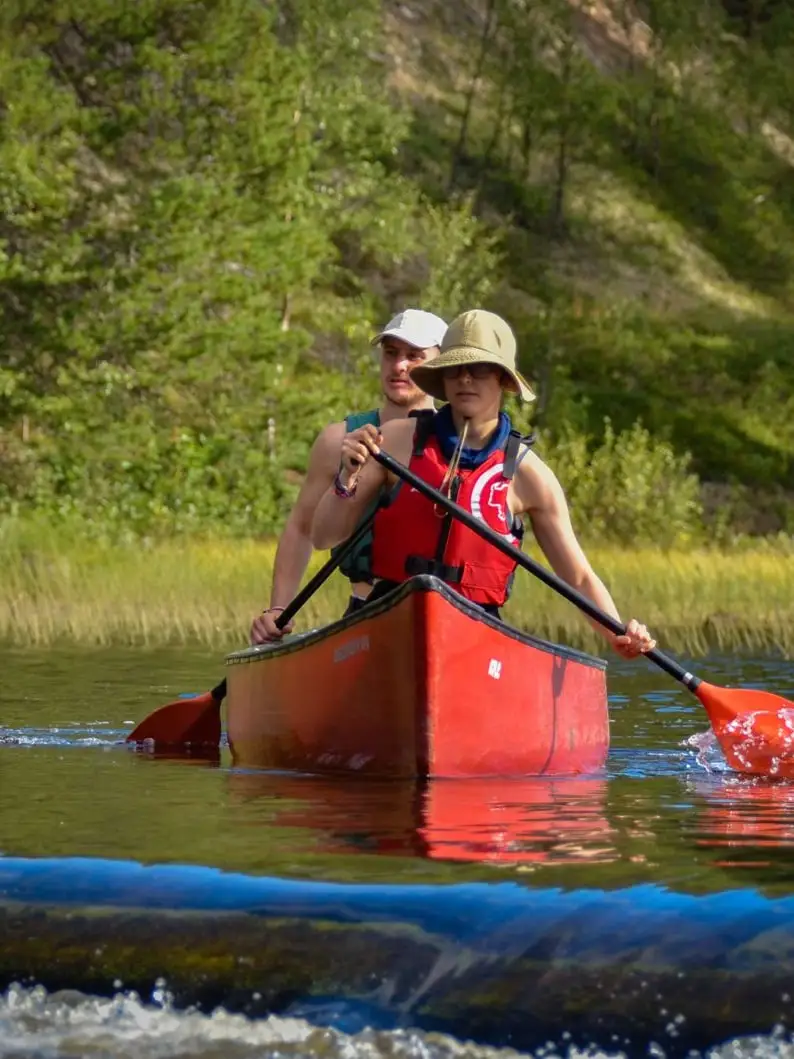 Two people paddling a red canoe on a river, forest along the bank