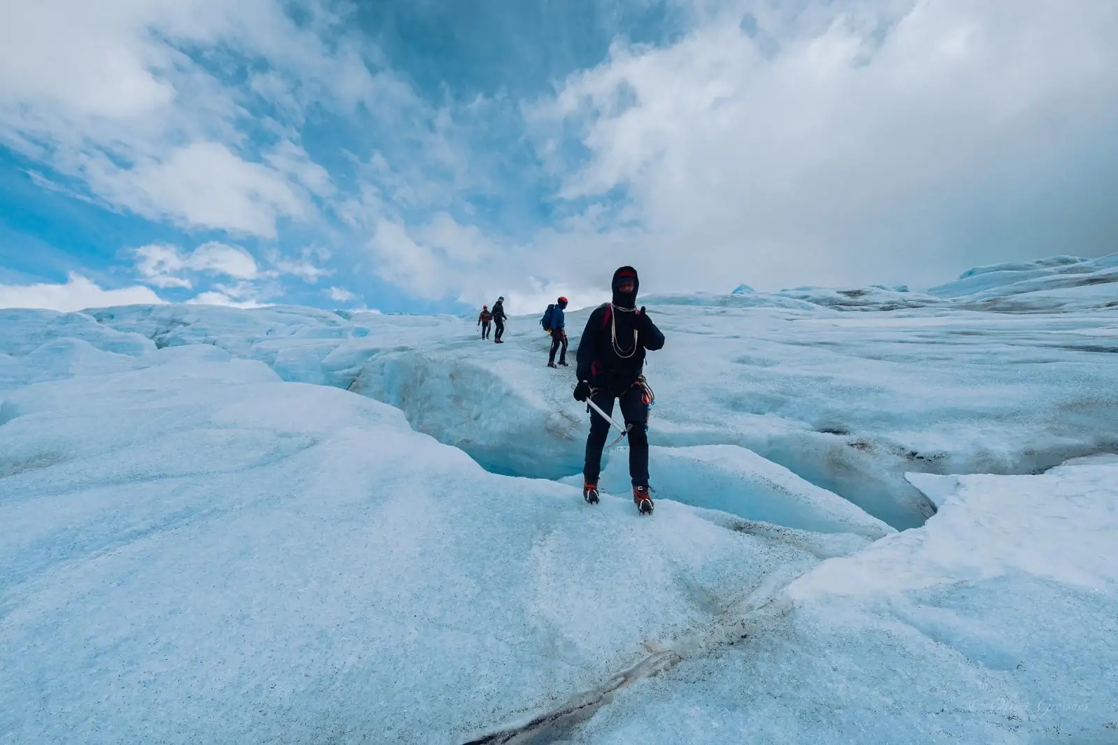 A roped team crossing blue glacier ice under a bright sky