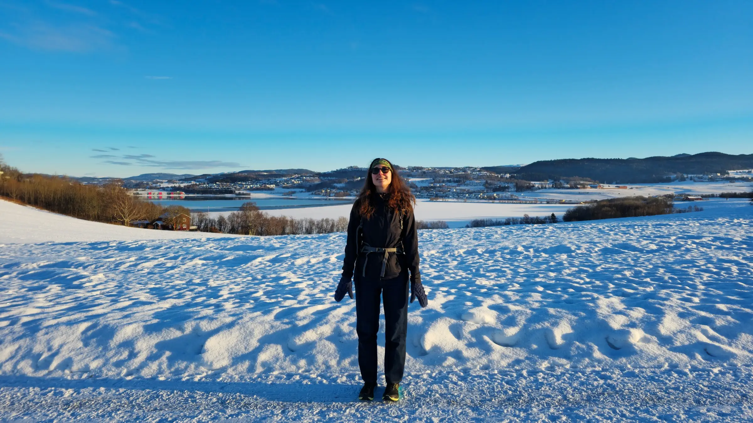Asia standing in deep snow above a frozen Norwegian valley, under a hard blue sky