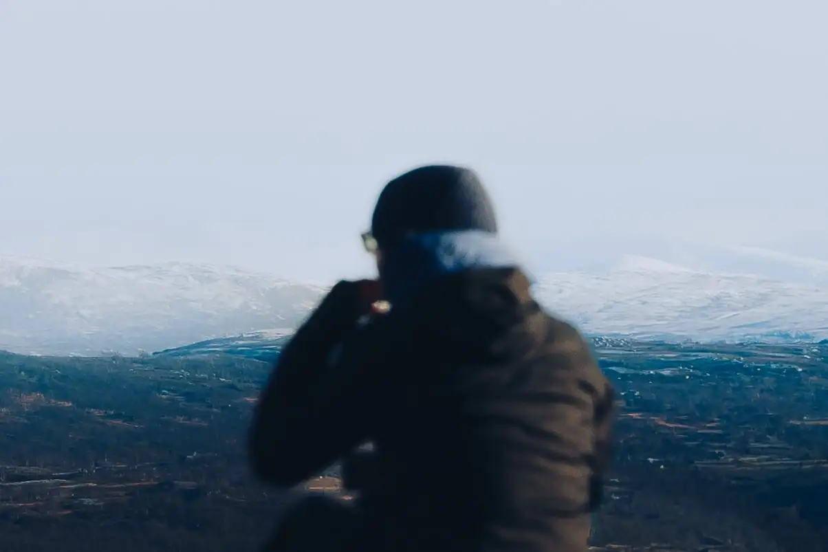 A figure in a down jacket looking out over snow-dusted Norwegian hills