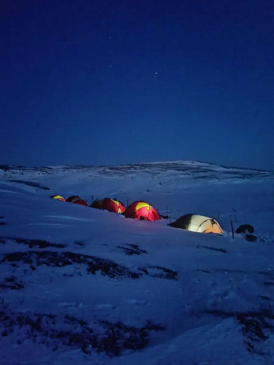 Four tents lit from the inside on a snowfield at blue hour